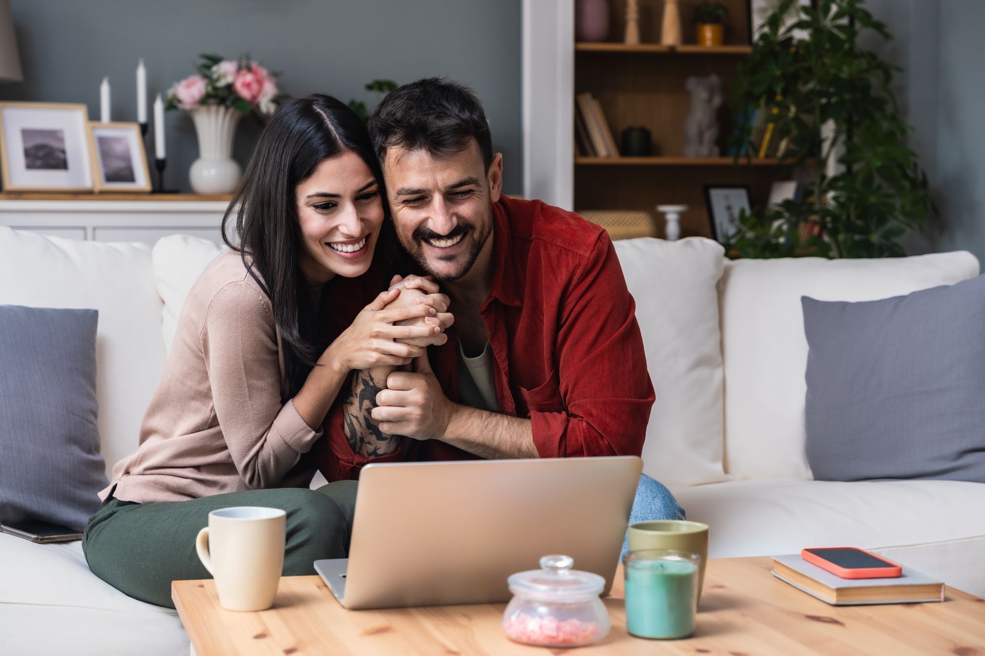 Smiling couple hugging on a couch in a cozy living room, with coffee cups on the table