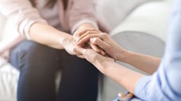Two people seated closely, holding hands in a supportive gesture indoors