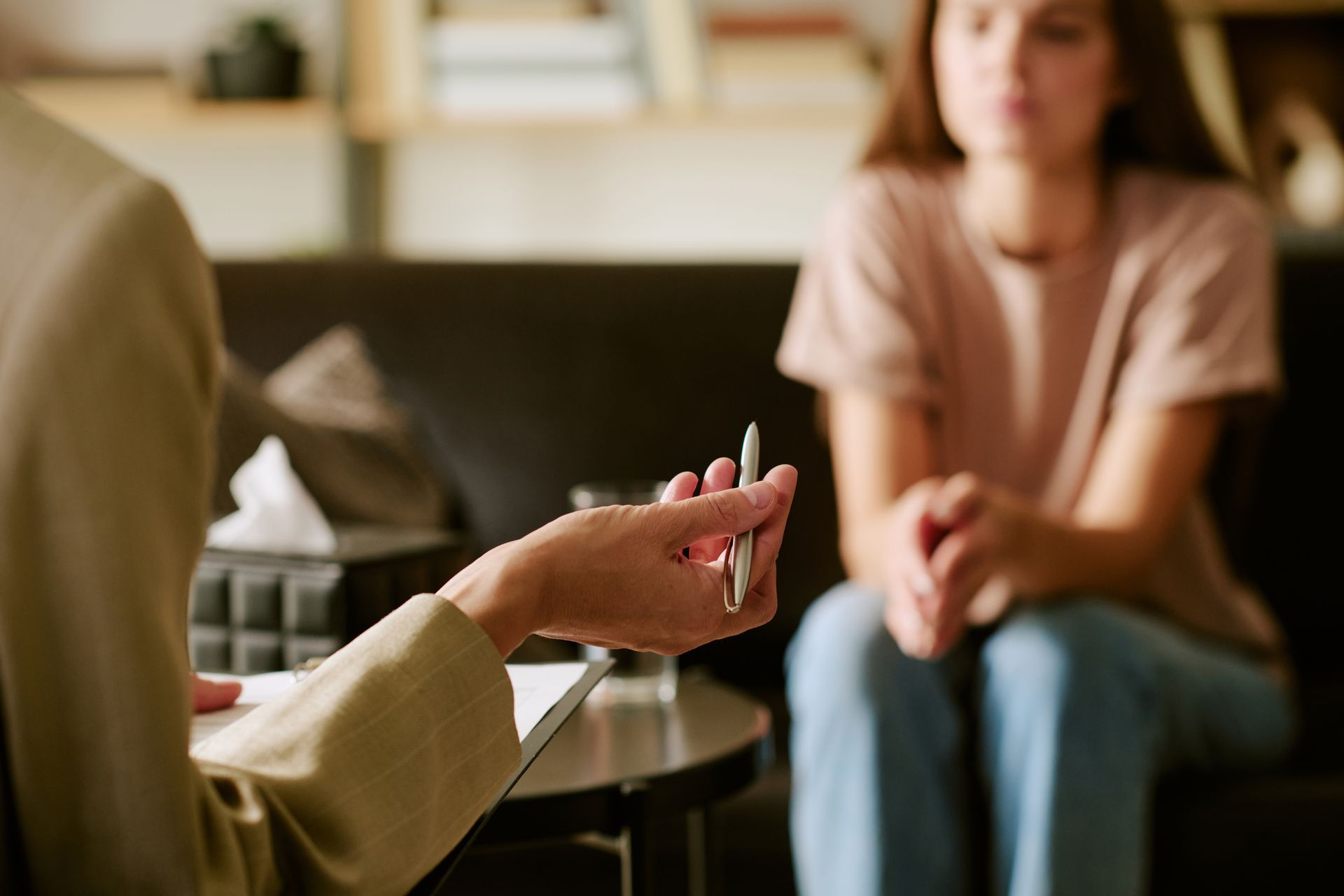Person gesturing during a conversation with another seated person in a softly lit room