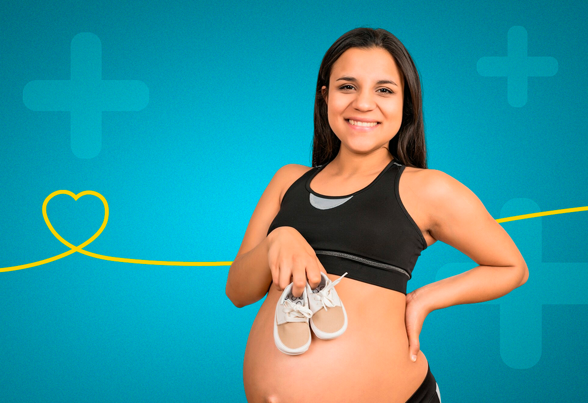A pregnant woman is holding a pair of baby shoes on her belly.