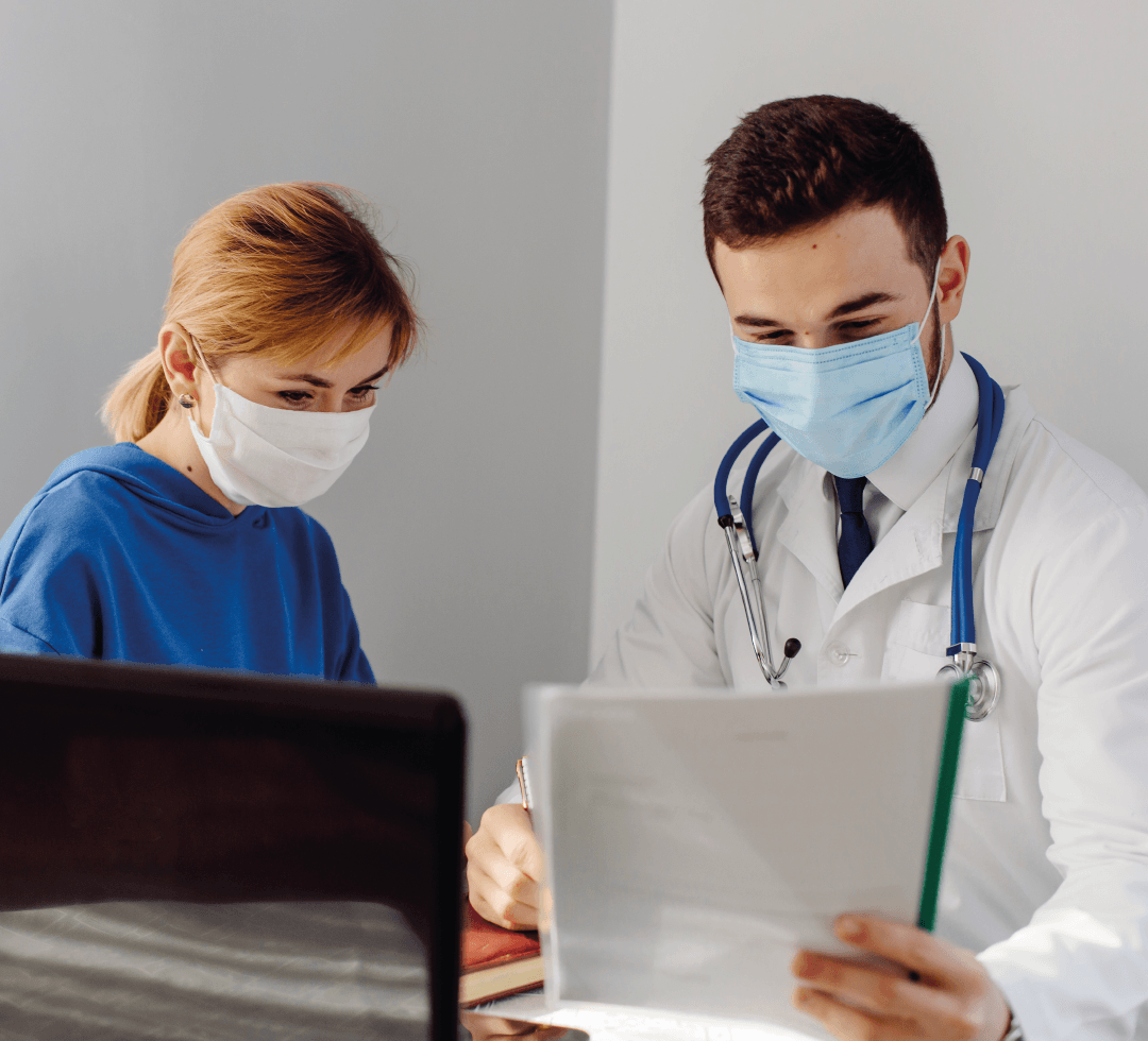 Criança com máscara sendo examinada por um médico, ambos em ambiente clínico.