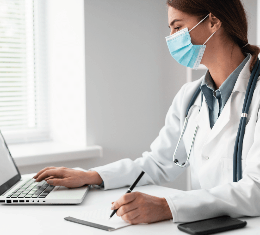 Profissional da saúde com máscara e estetoscópio usando laptop, simbolizando cotação ou atendimento online de plano de saúde.