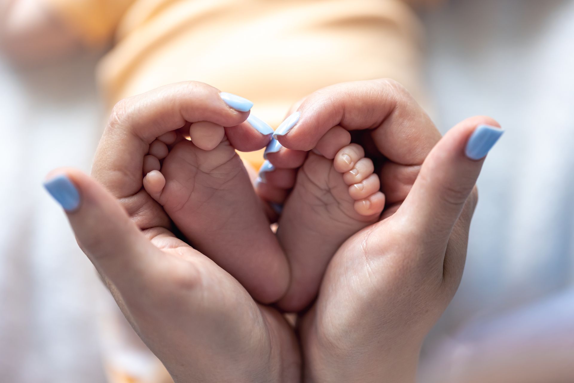 A woman is holding a baby 's feet in her hands in the shape of a heart.