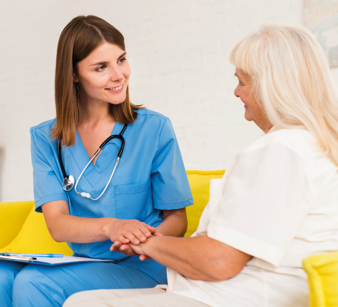 Duas profissionais de saúde sorrindo, uma delas com estetoscópio, sentadas e conversando com paciente.