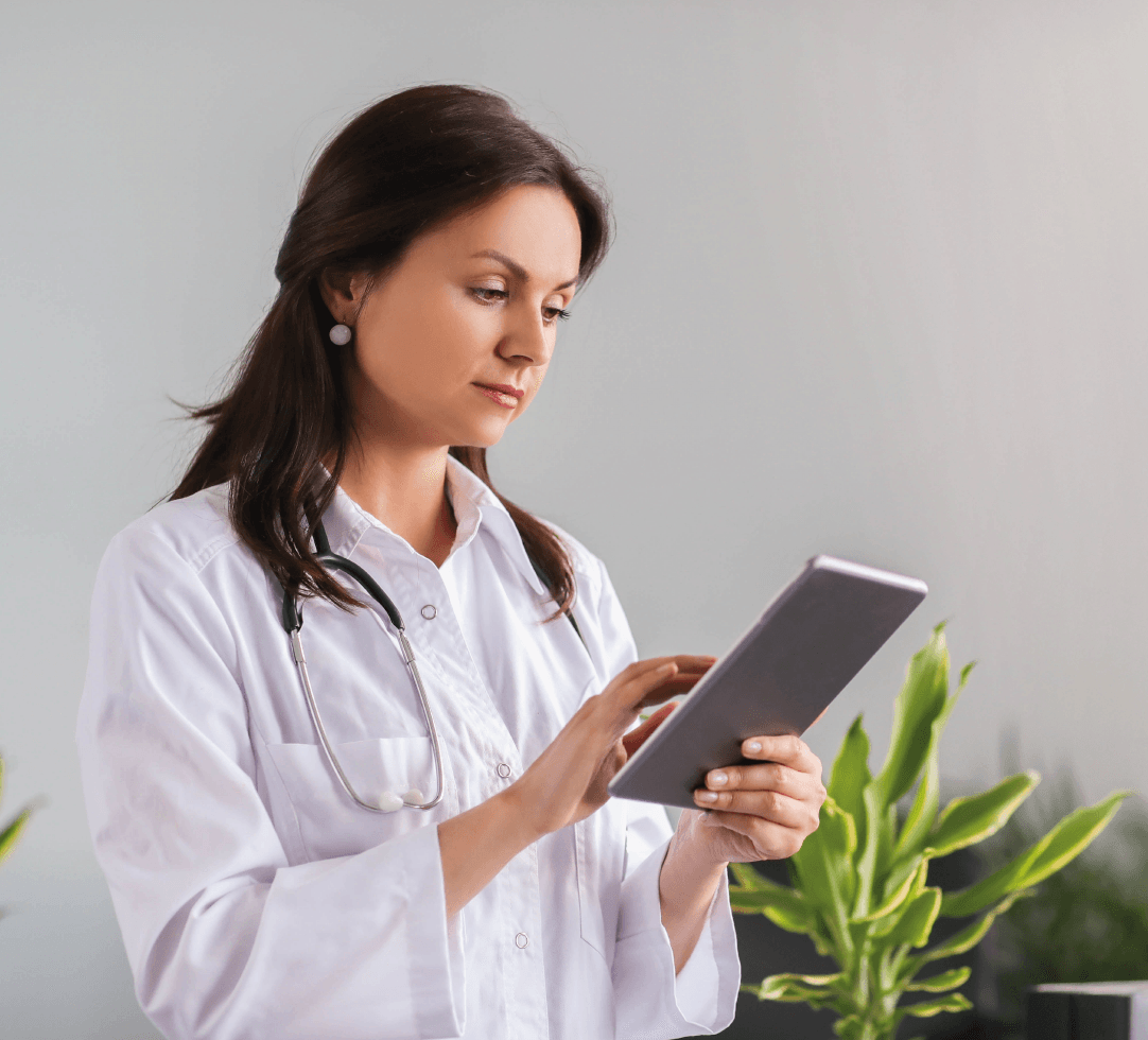 Profissional da saúde usando jaleco branco consulta informações em um tablet, com plantas ao fundo