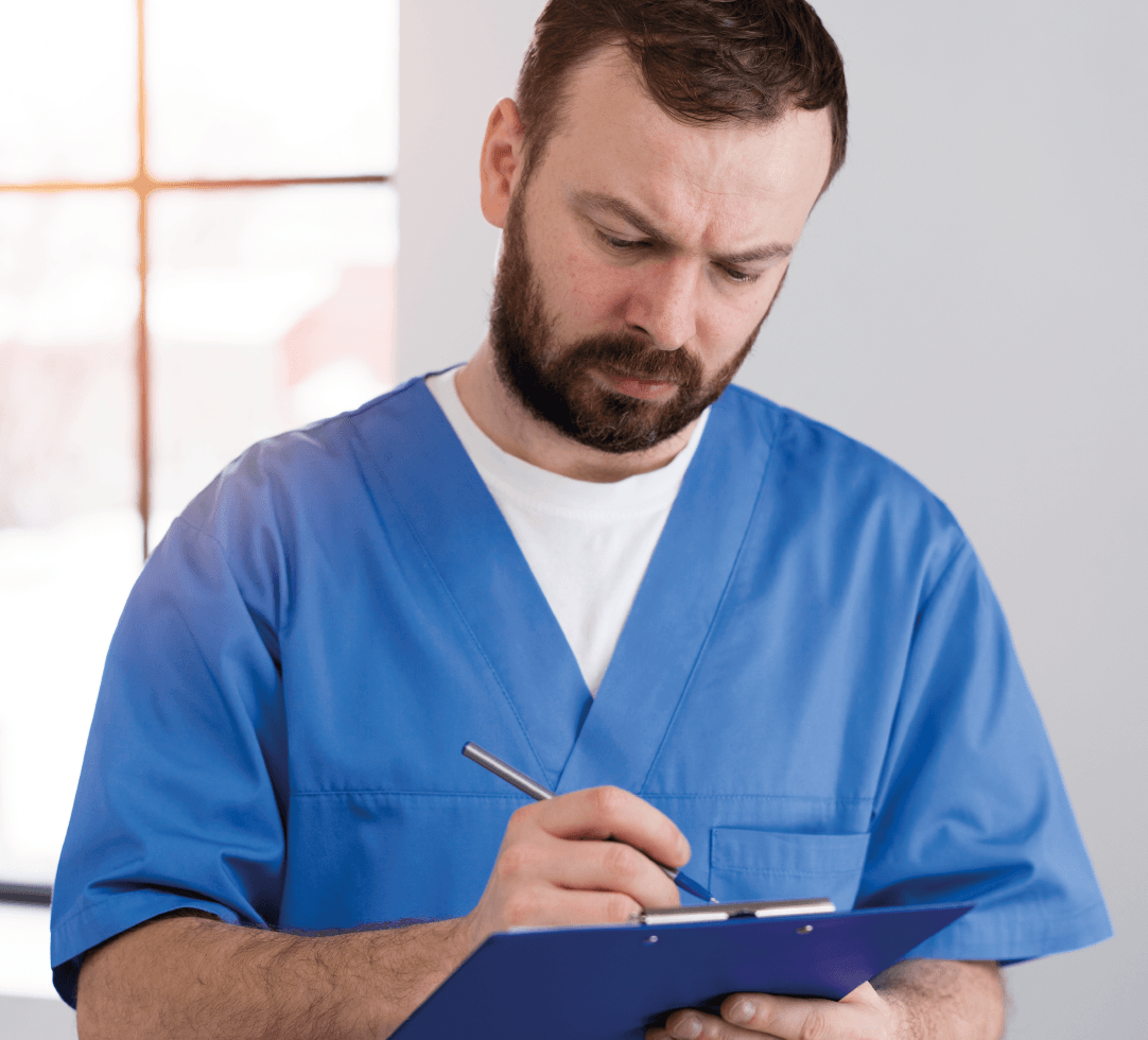 Homem com barba vestindo uniforme médico azul, olhando para baixo com expressão concentrada.