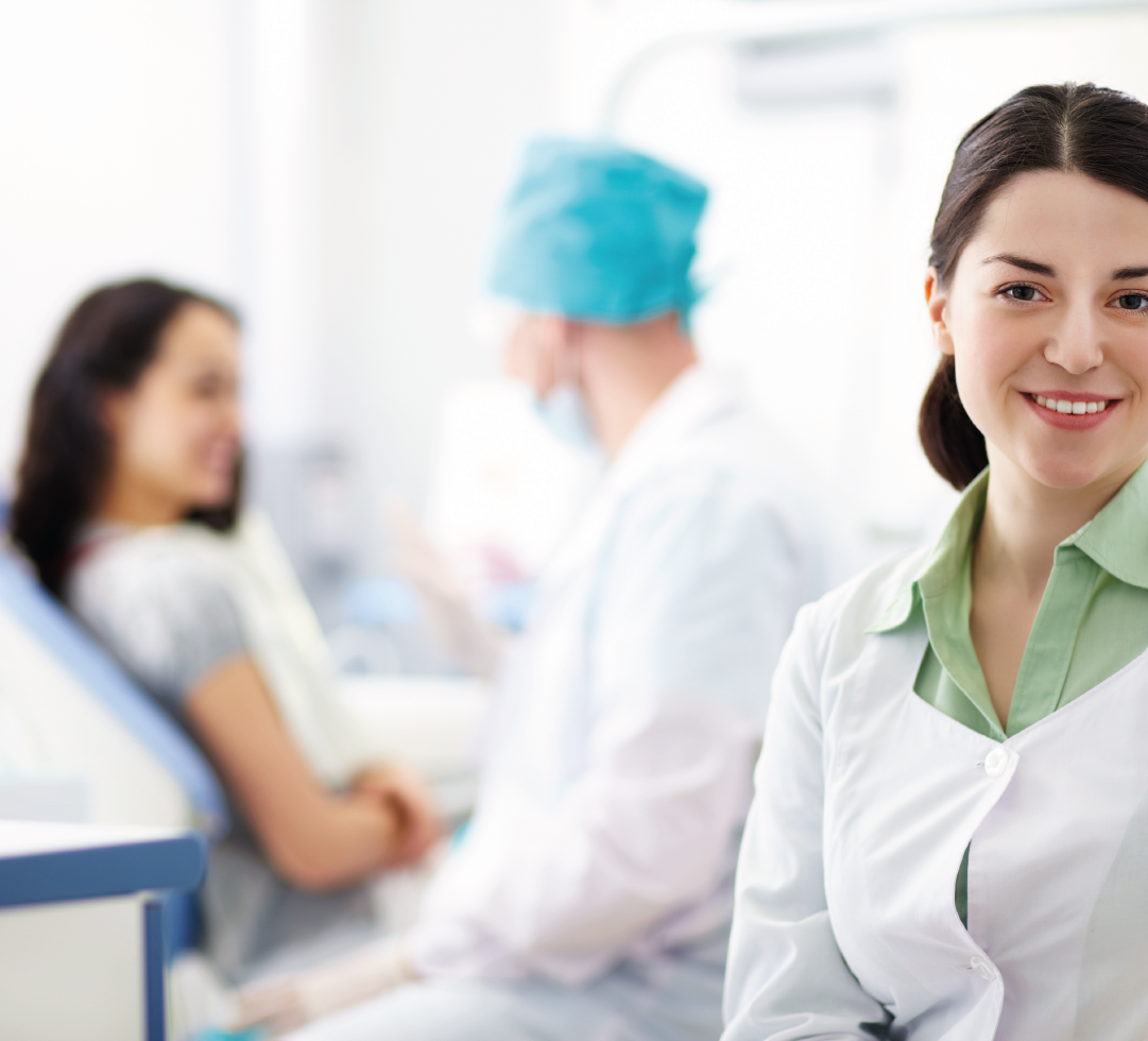 Mulher sorridente de jaleco médico ao lado de paciente em ambiente hospitalar, simbolizando atendimento humanizado.