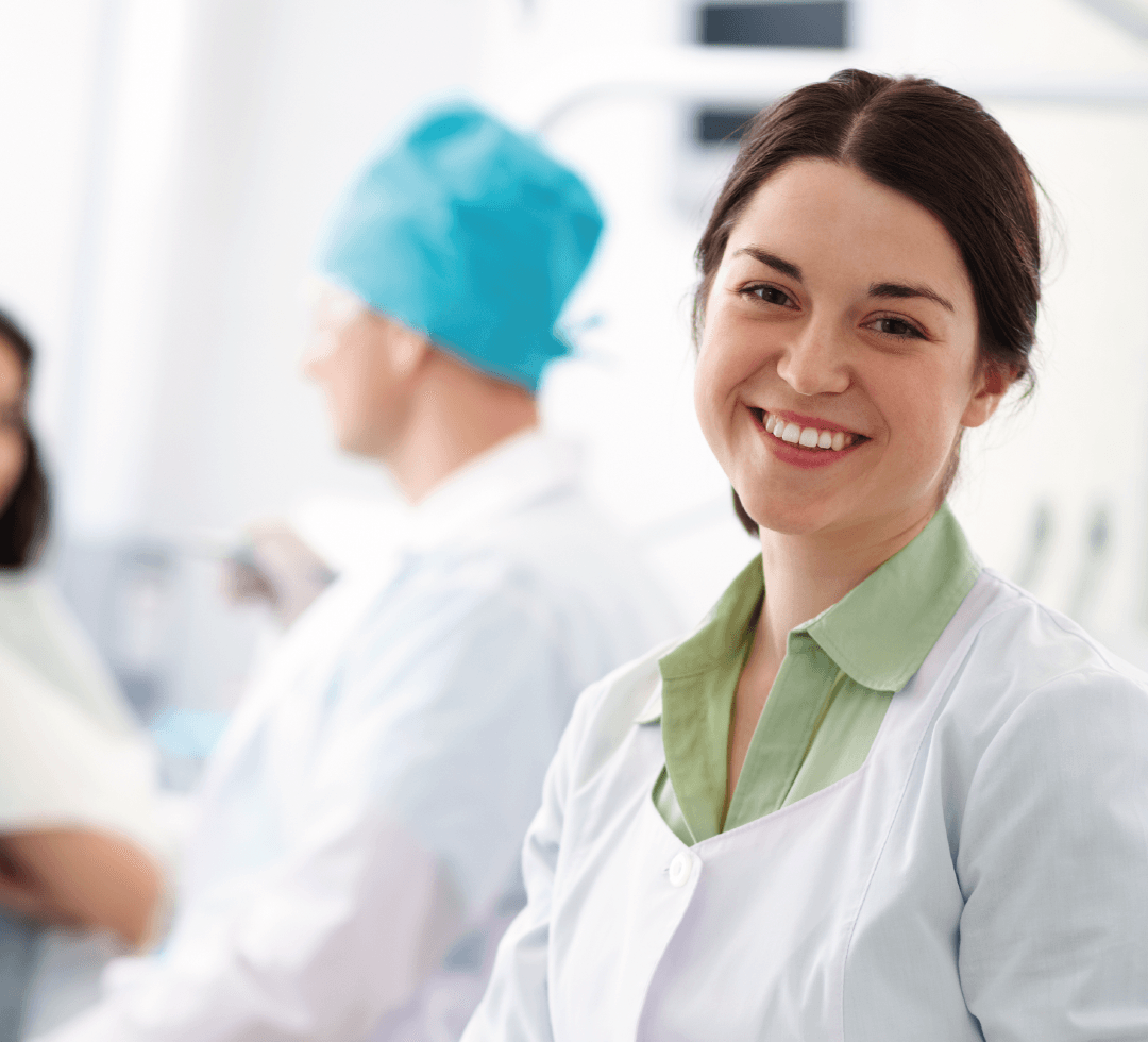 Mulher de jaleco sorrindo em ambiente hospitalar, transmitindo confiança e acolhimento.