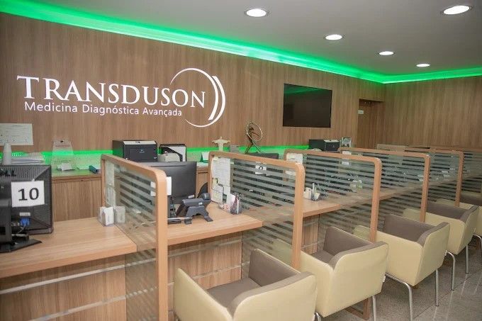 Uma fileira de cubículos com cadeiras e computadores em um consultório médico.