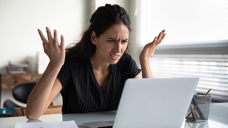 A woman is sitting at a desk looking at a laptop computer.