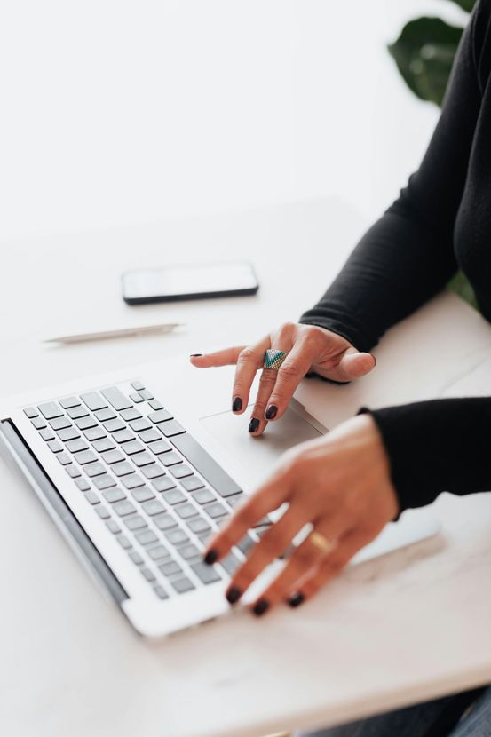 A woman is typing on a laptop computer at a desk.