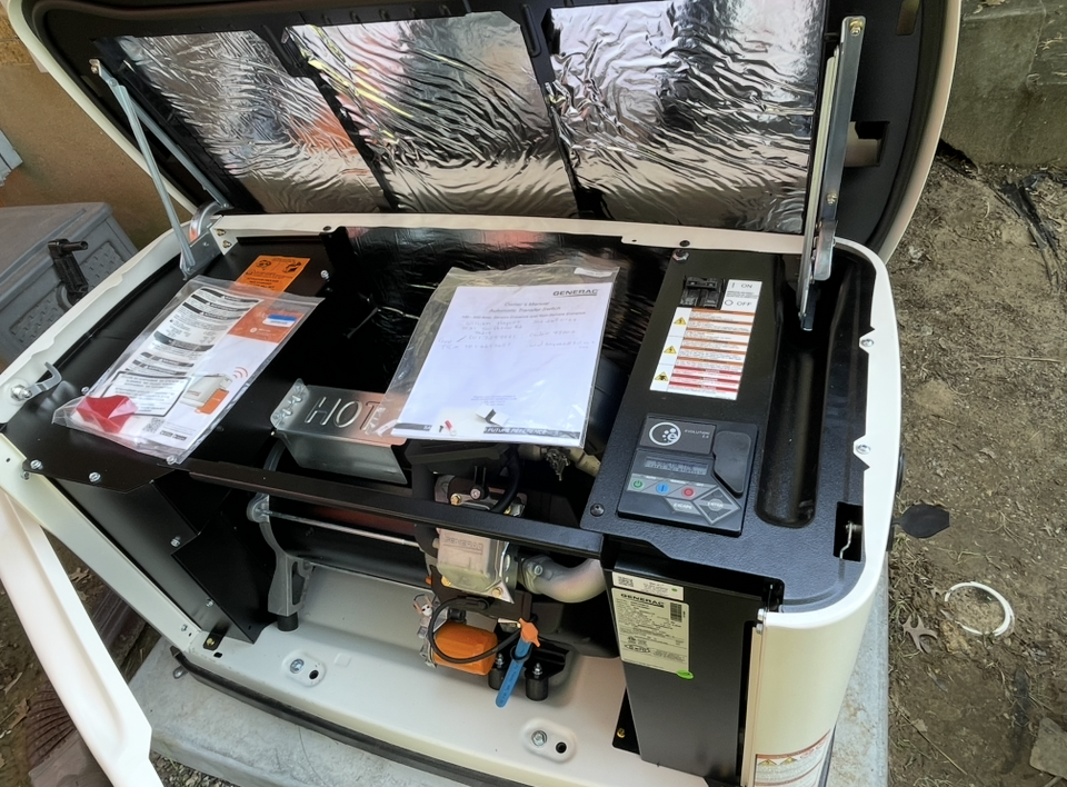 A generator is sitting in the dirt next to a building.