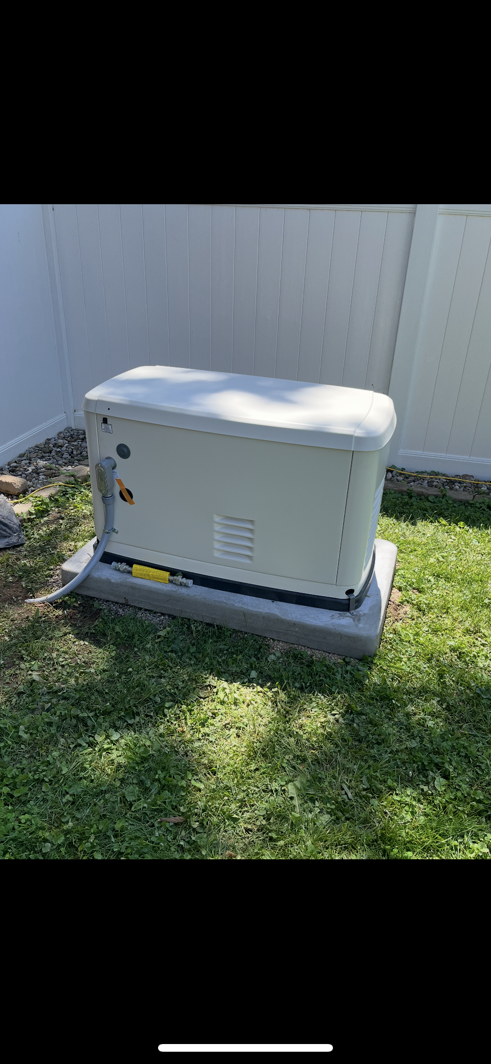 A white generator is sitting outside of a house.