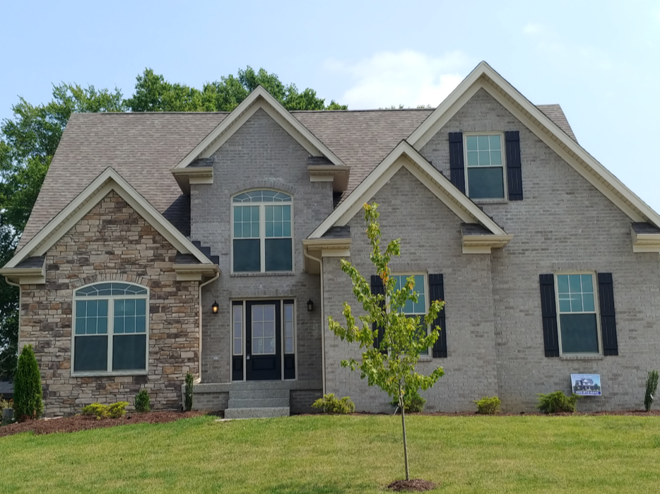 A large house with a large deck in the middle of a lush green field.