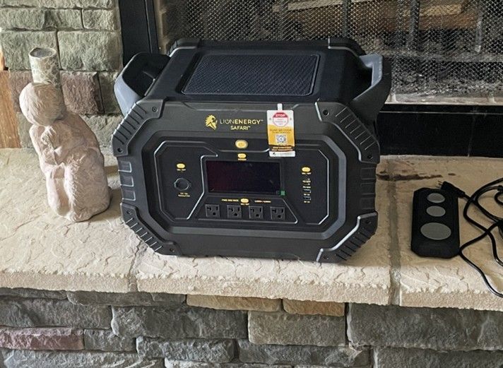Black power station with a screen and outlets, next to a small statue on a brick surface. Black power station with a screen and outlets, next to a small statue on a brick surface.