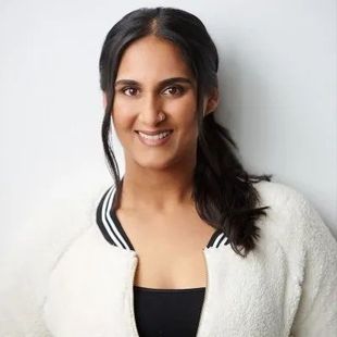 A woman wearing a white jacket and a black top is smiling for the camera.