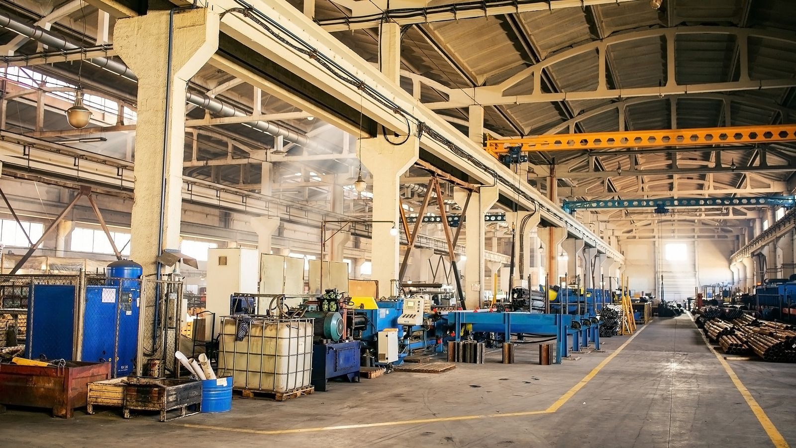 Industrial factory interior with machinery, overhead crane, and long yellow lines.
