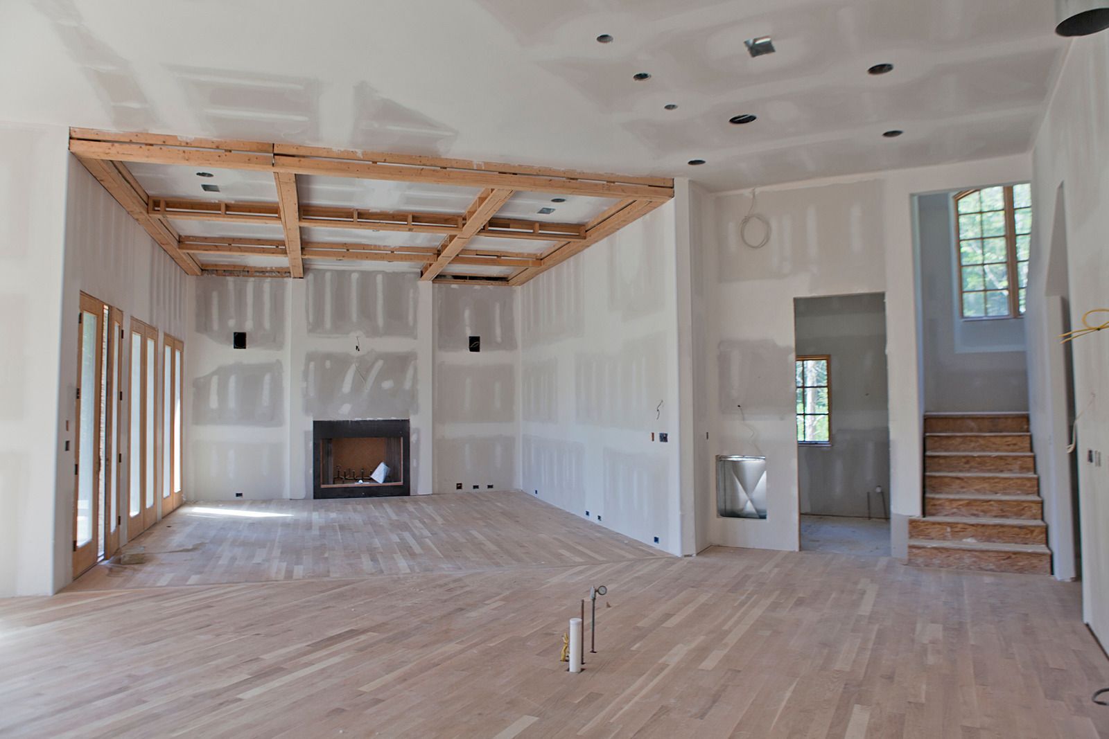 Interior of a home under construction; drywall walls, wood beams, unfinished wood floor, fireplace.