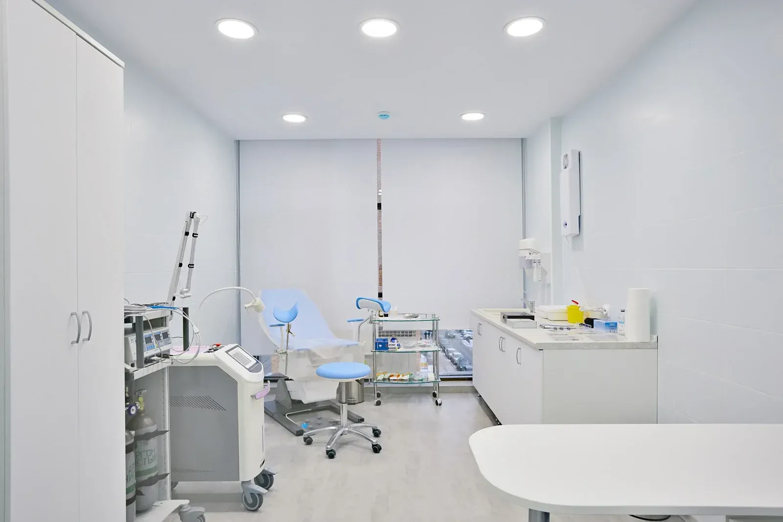 Medical examination room: Light blue exam chair, white cabinets, medical equipment, and bright lighting.