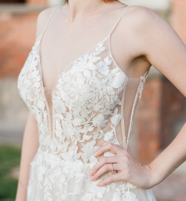 White lace wedding dress with floral details and thin straps, shown on a woman with hand on hip.