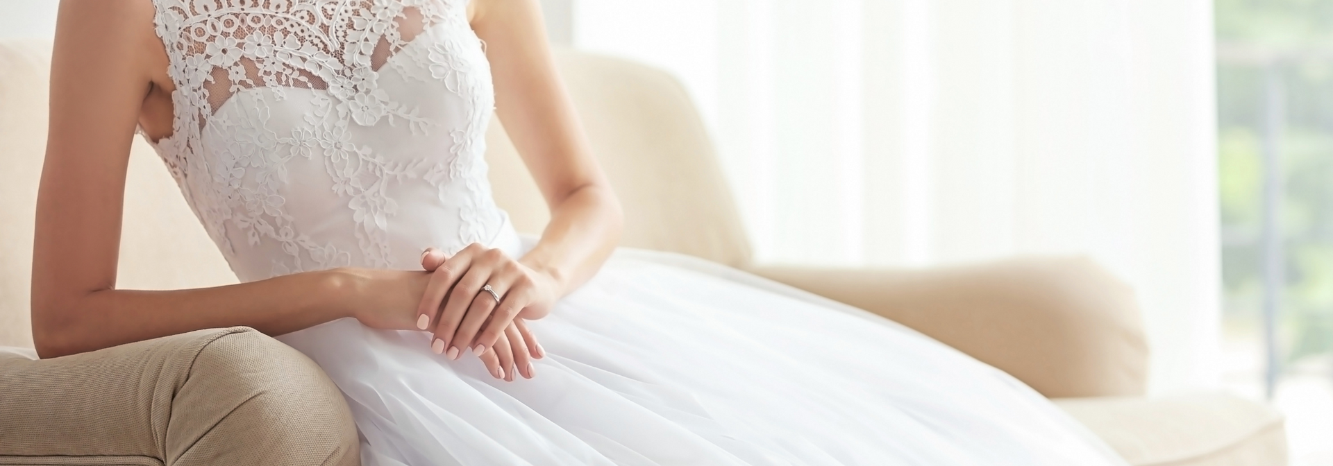 Bride in a white lace wedding dress sitting on a couch with hands resting in her lap