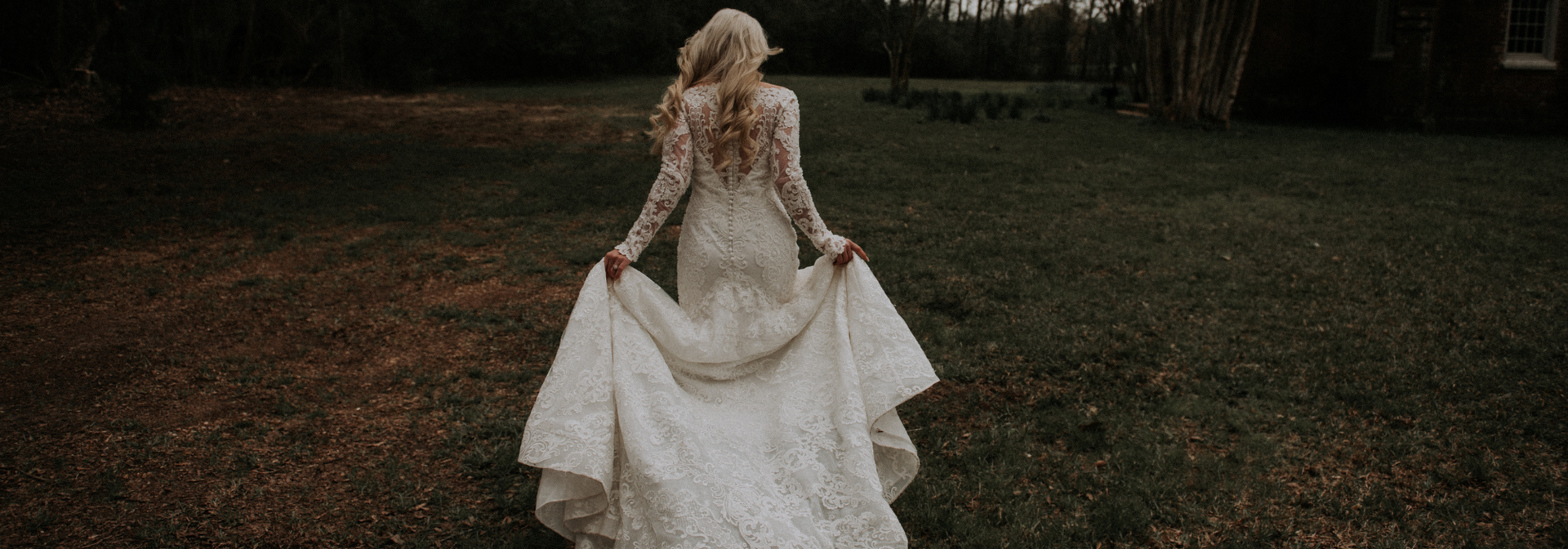 Person in a white dress walking away through a dark grassy field at dusk.