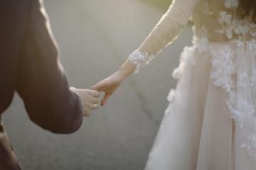 Two people holding hands during a wedding ceremony, with a bride in a white dress