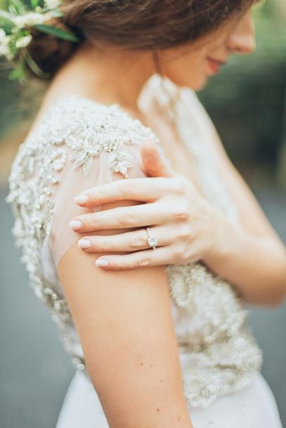 Woman in white lace dress touching her shoulder, showing a ring on her hand.