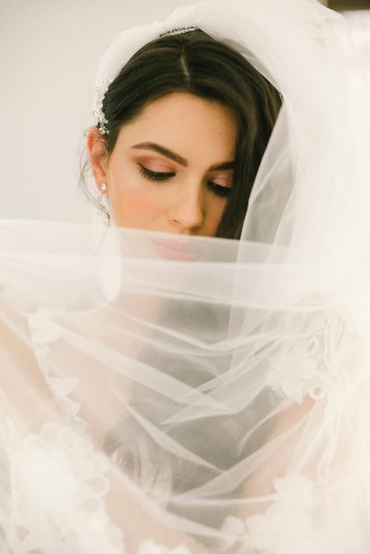 Bride with dark hair and a white veil, eyes closed against a soft white background