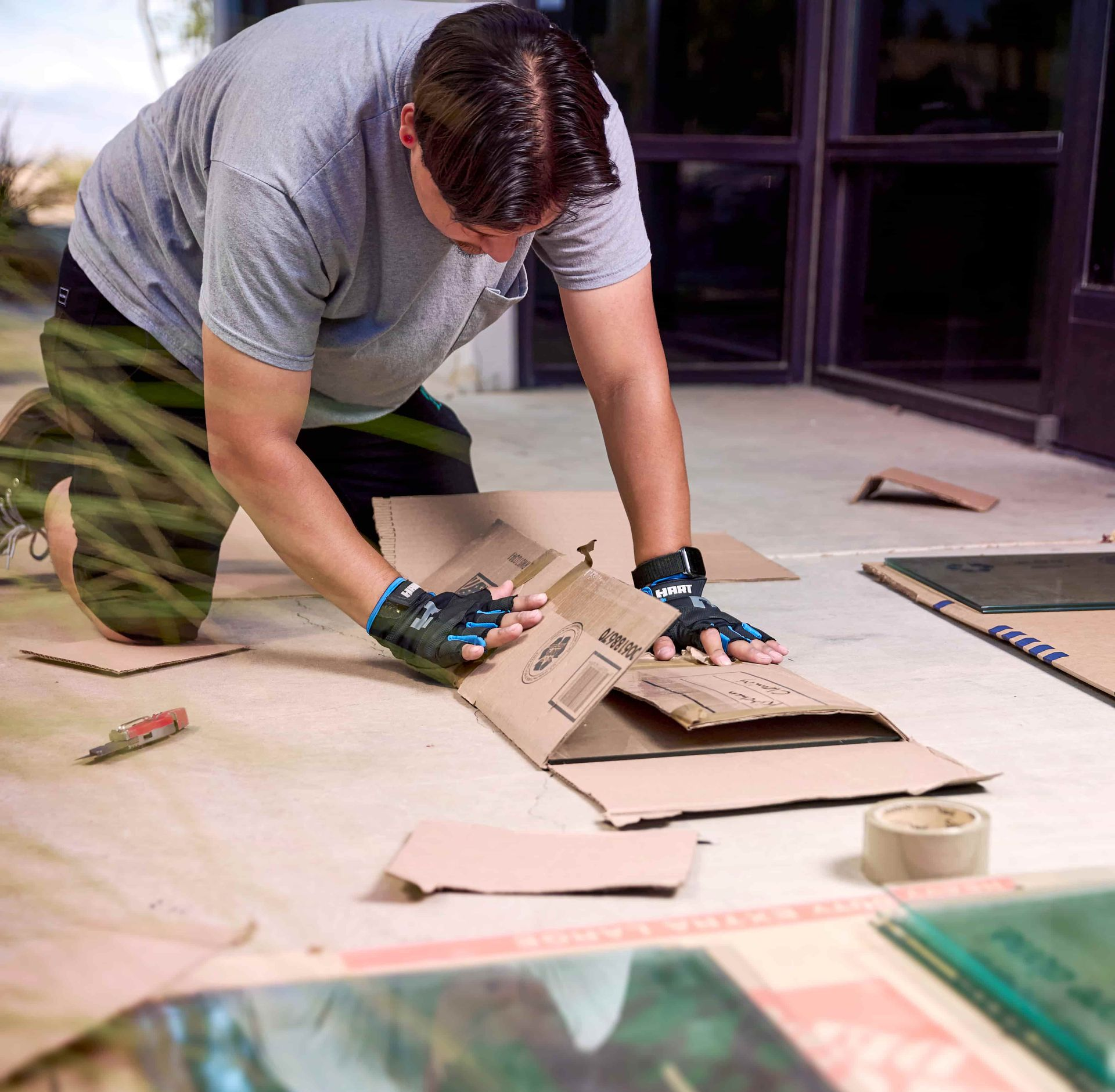 Person kneeling, preparing protective cardboard for glass sheets on a floor, wearing gloves.