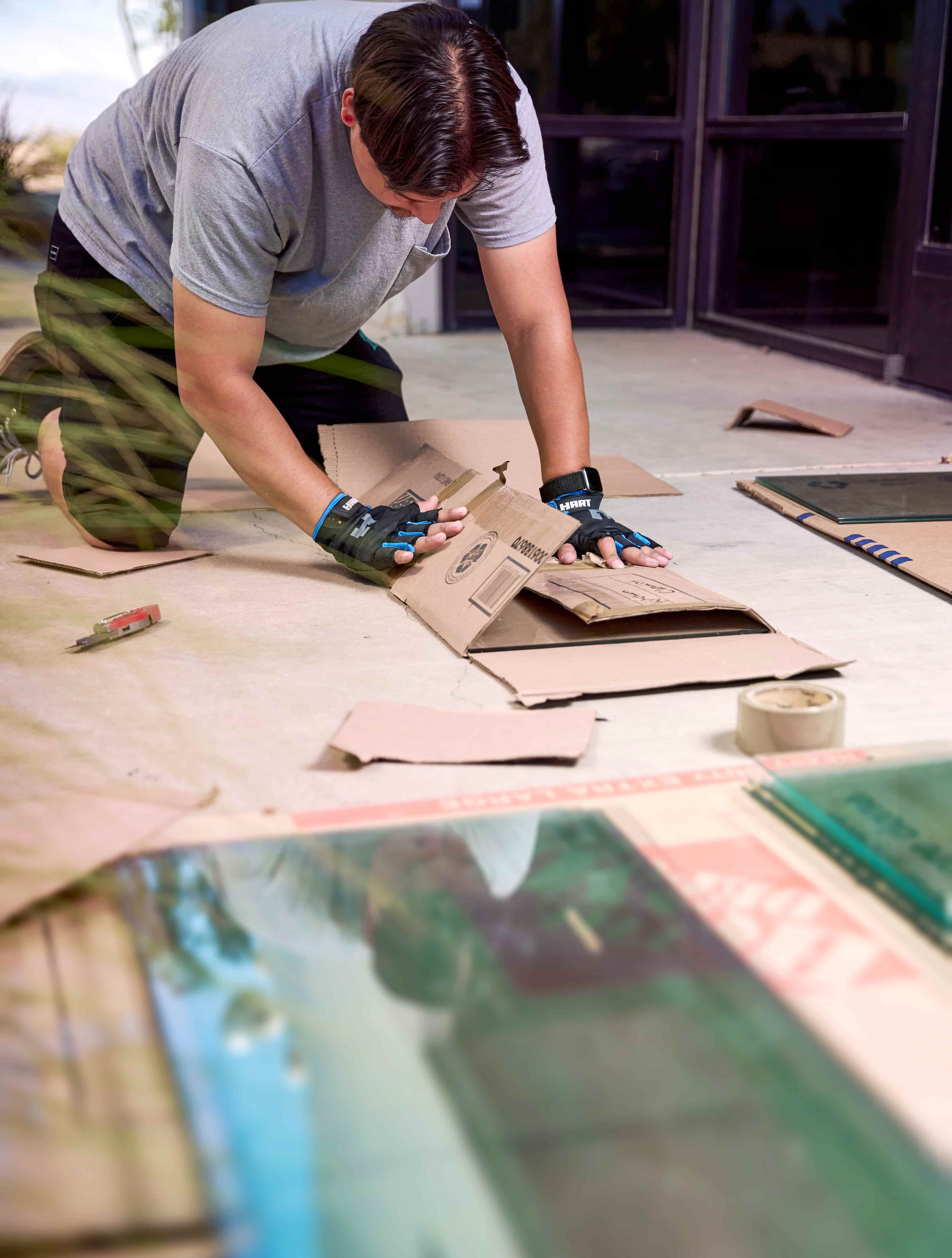 Person kneeling, preparing protective cardboard for glass sheets on a floor, wearing gloves.
