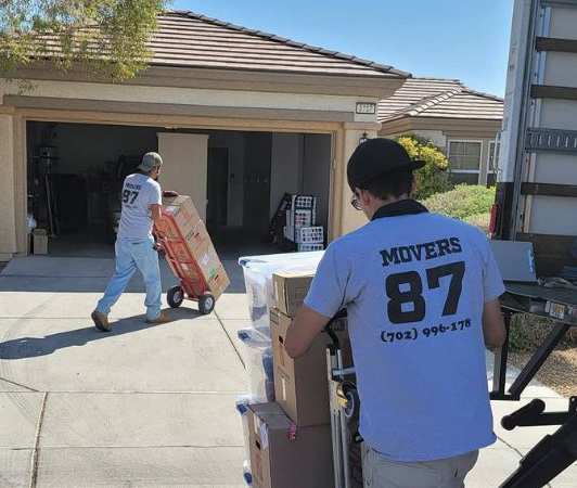 Movers loading boxes and furniture from a home into a truck on a sunny day.