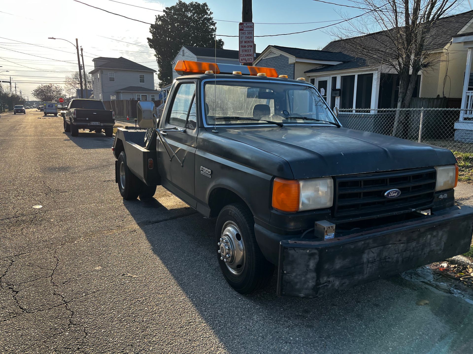 A matte black Ford dually pickup truck with amber warning lights, parked on a residential street.
