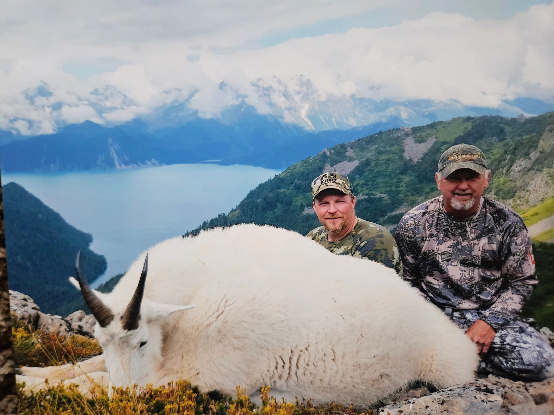 Two men posing with a dead mountain goat on top of a mountain