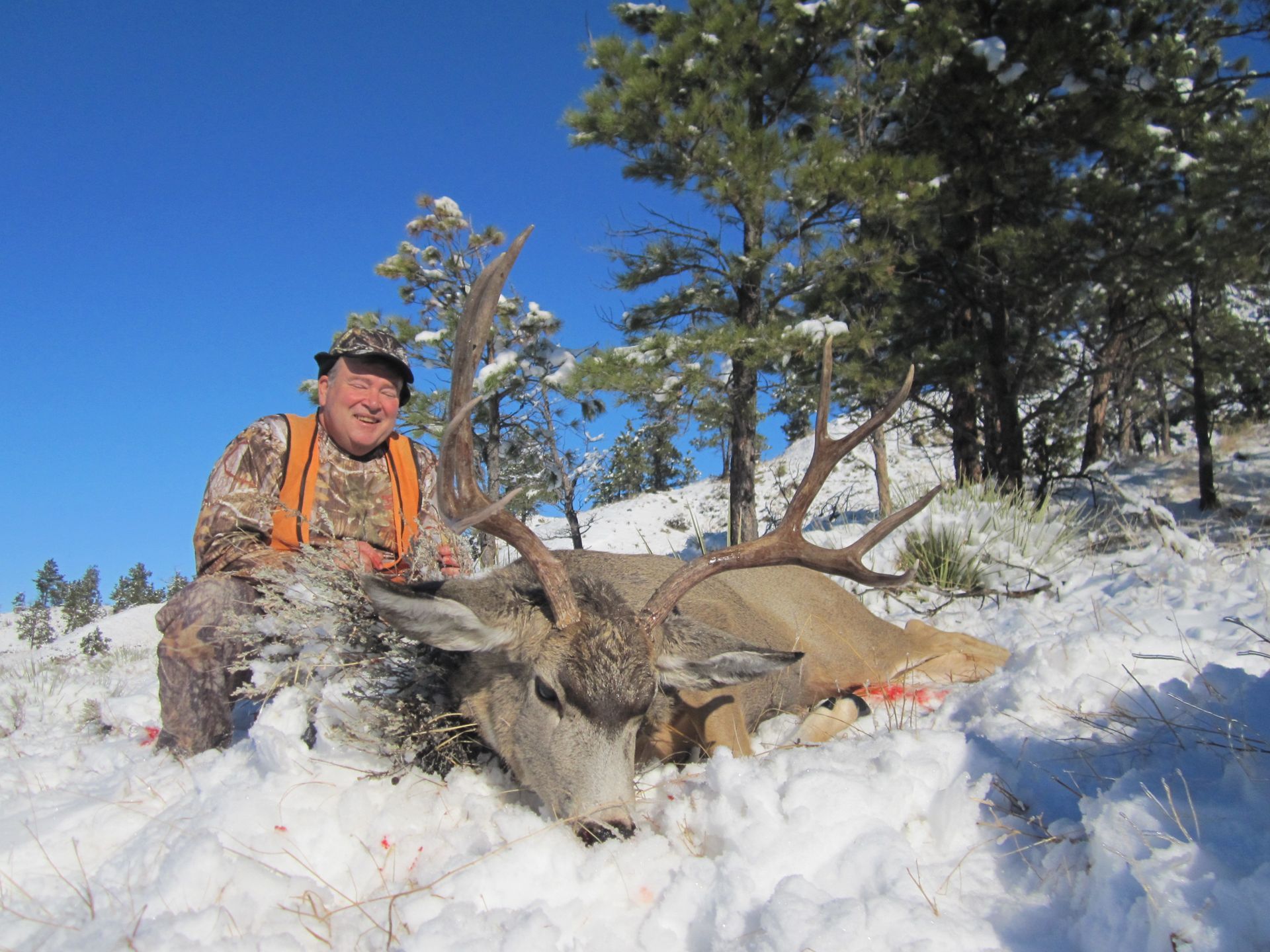 A man posing in the snow with a dead deer