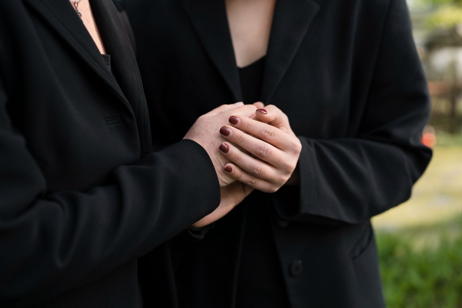 Two people in black suits holding hands.