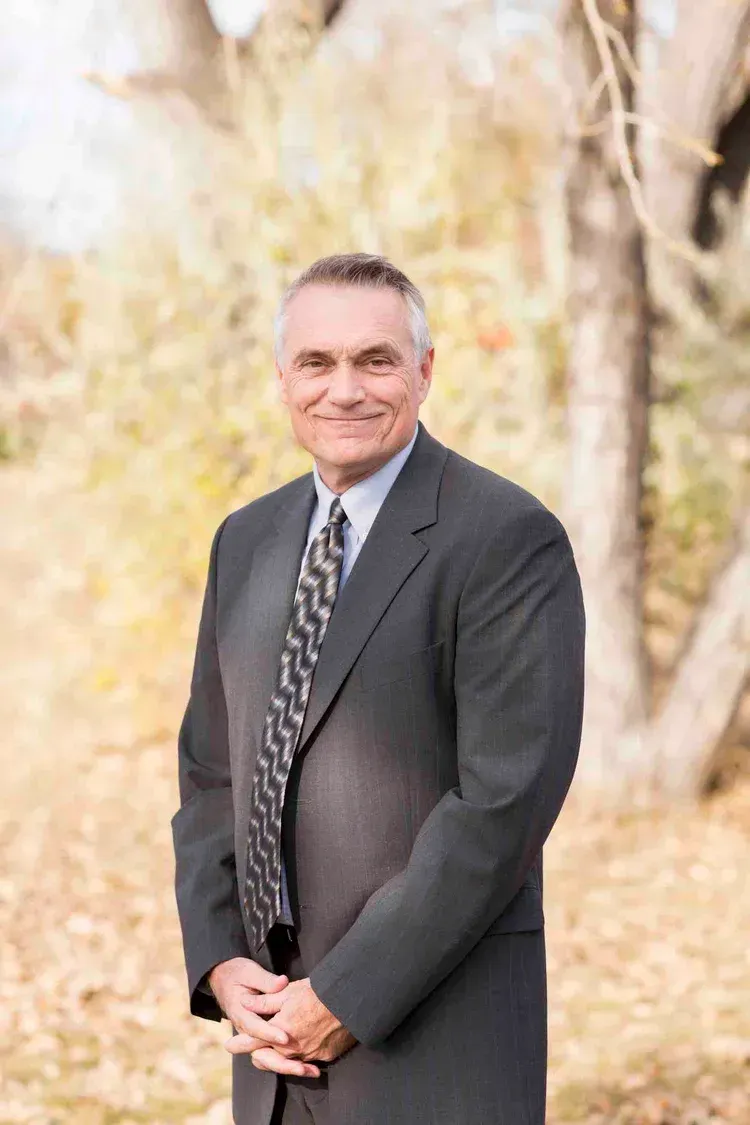 Man in a suit, smiling, arms crossed, standing outdoors.