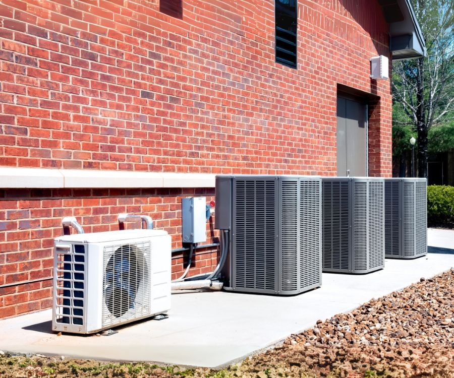 A row of air conditioners are sitting outside of a brick building.