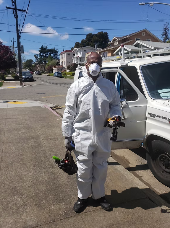 A man wearing a protective suit and mask is standing in front of a white van.