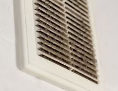 A close up of a dirty air vent on a wall.