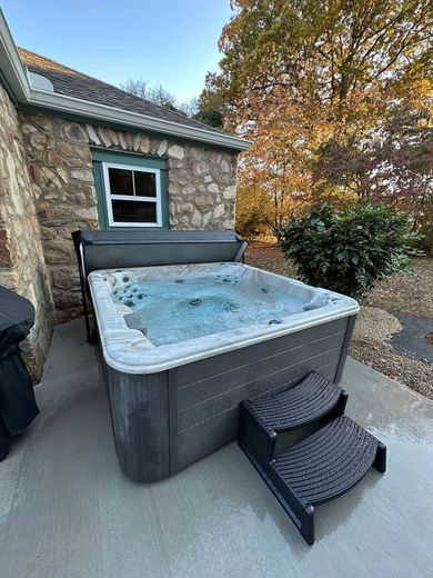 Hot tub with bubbling water on a concrete patio next to a stone building with a small window. Hot tub with bubbling water on a concrete patio next to a stone building with a small window.