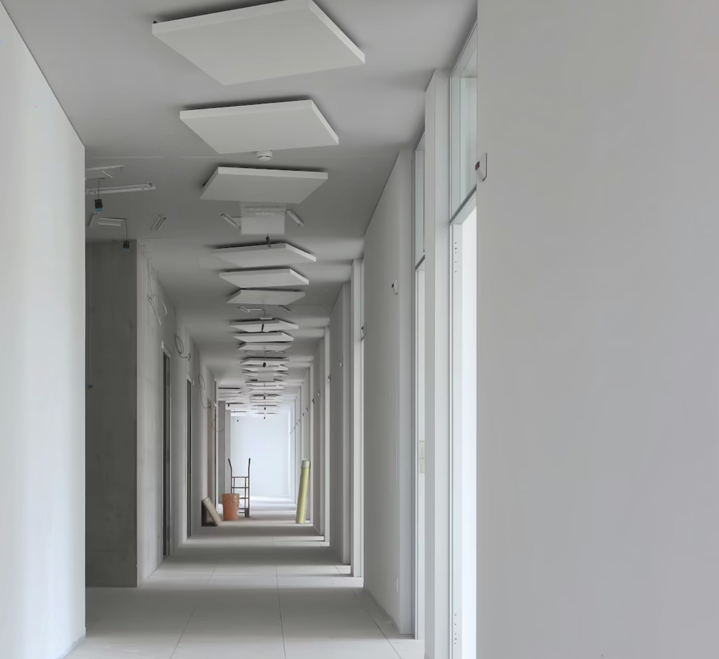 Un lungo corridoio minimalista con pareti bianche e una serie di lampade a soffitto di forma quadrata che conduce a un'uscita luminosa.