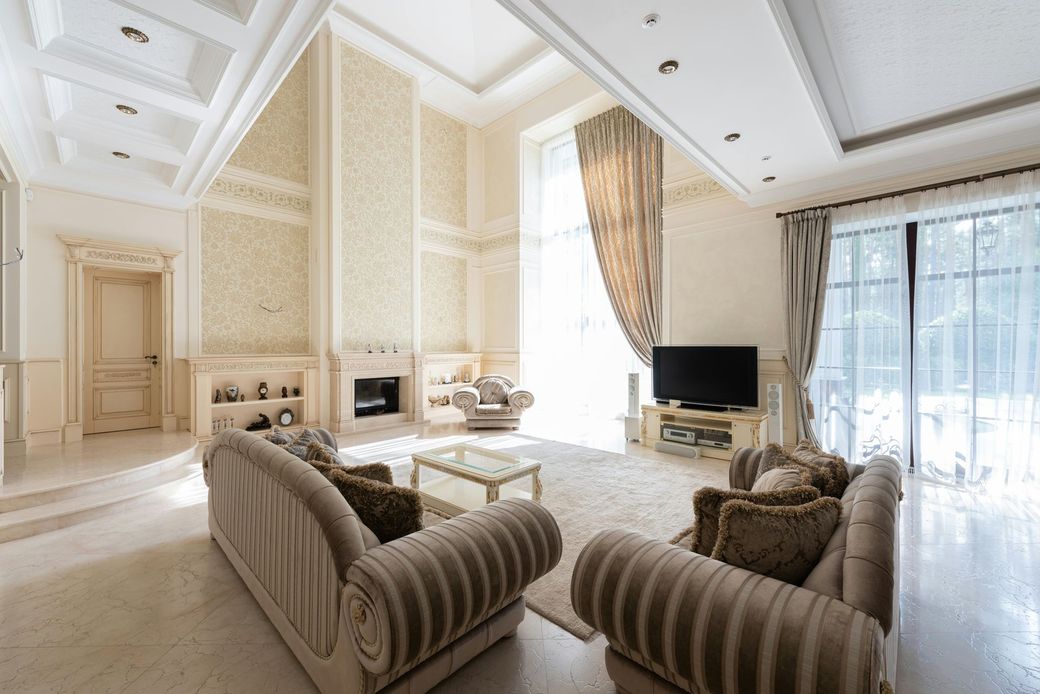 Elegant living room with beige sofas, fireplace, tall windows, and intricate wall detailing.