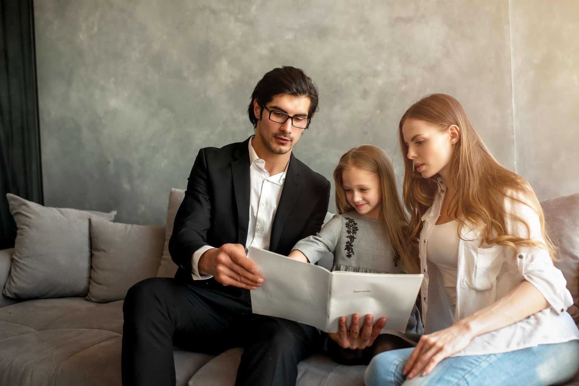 A man in a suit is sitting on a couch with a woman and a little girl.