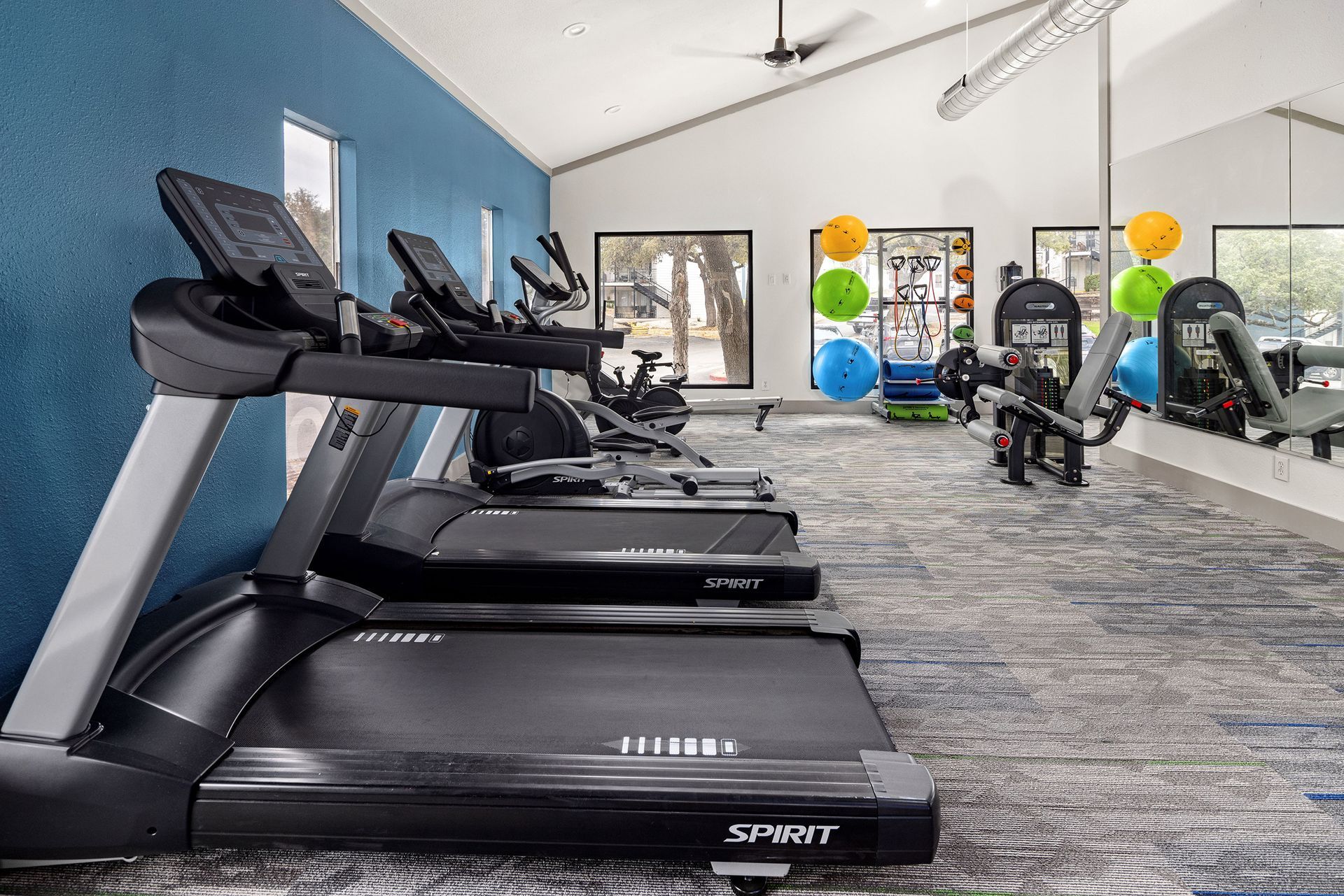 a gym with treadmills, exercise bikes, and a ceiling fan.
