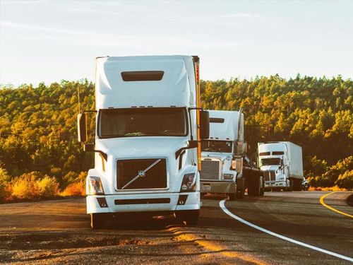 A row of semi trucks are driving down a highway.