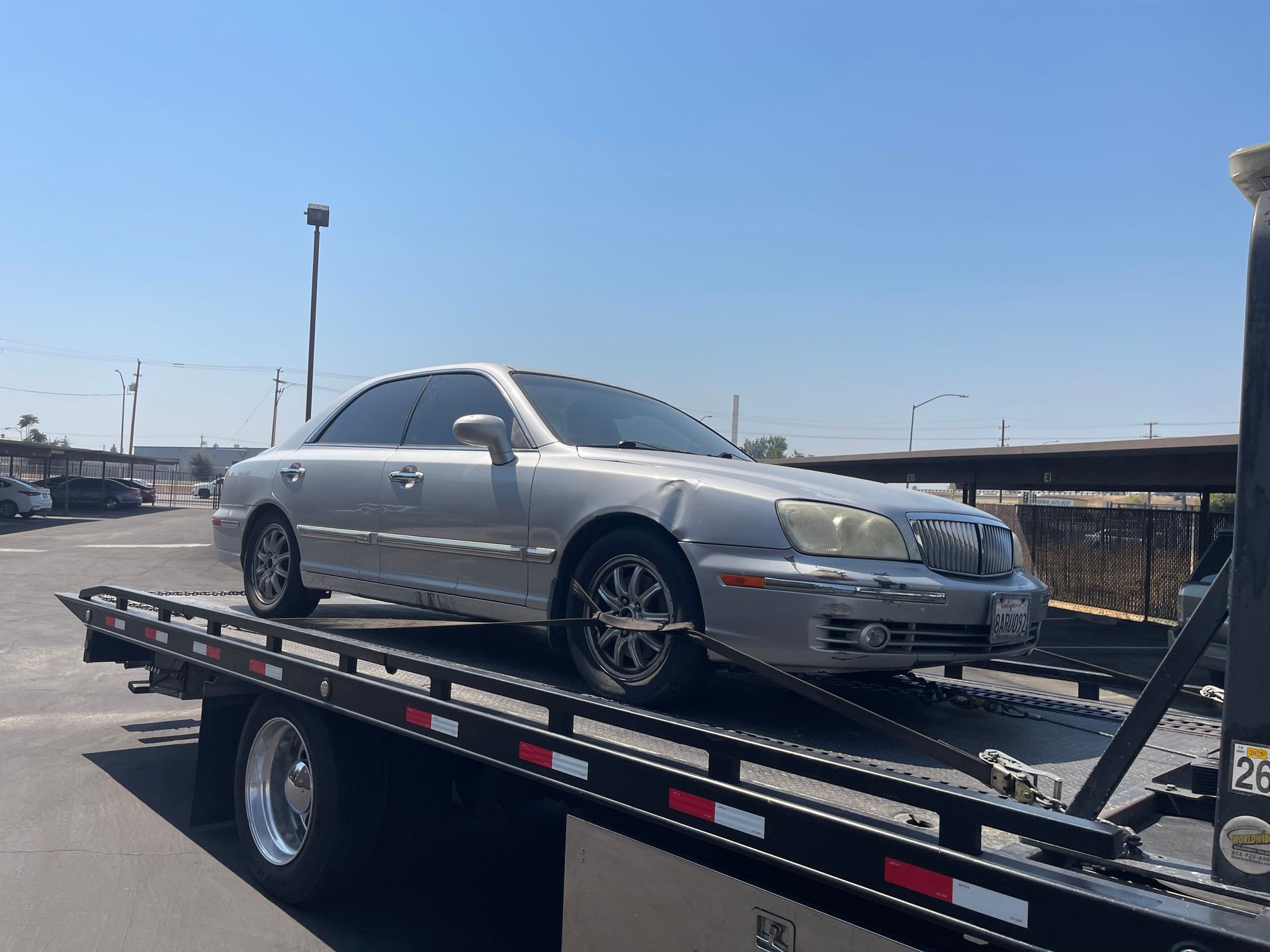 Silver sedan on a flatbed tow truck outdoors on a sunny day.