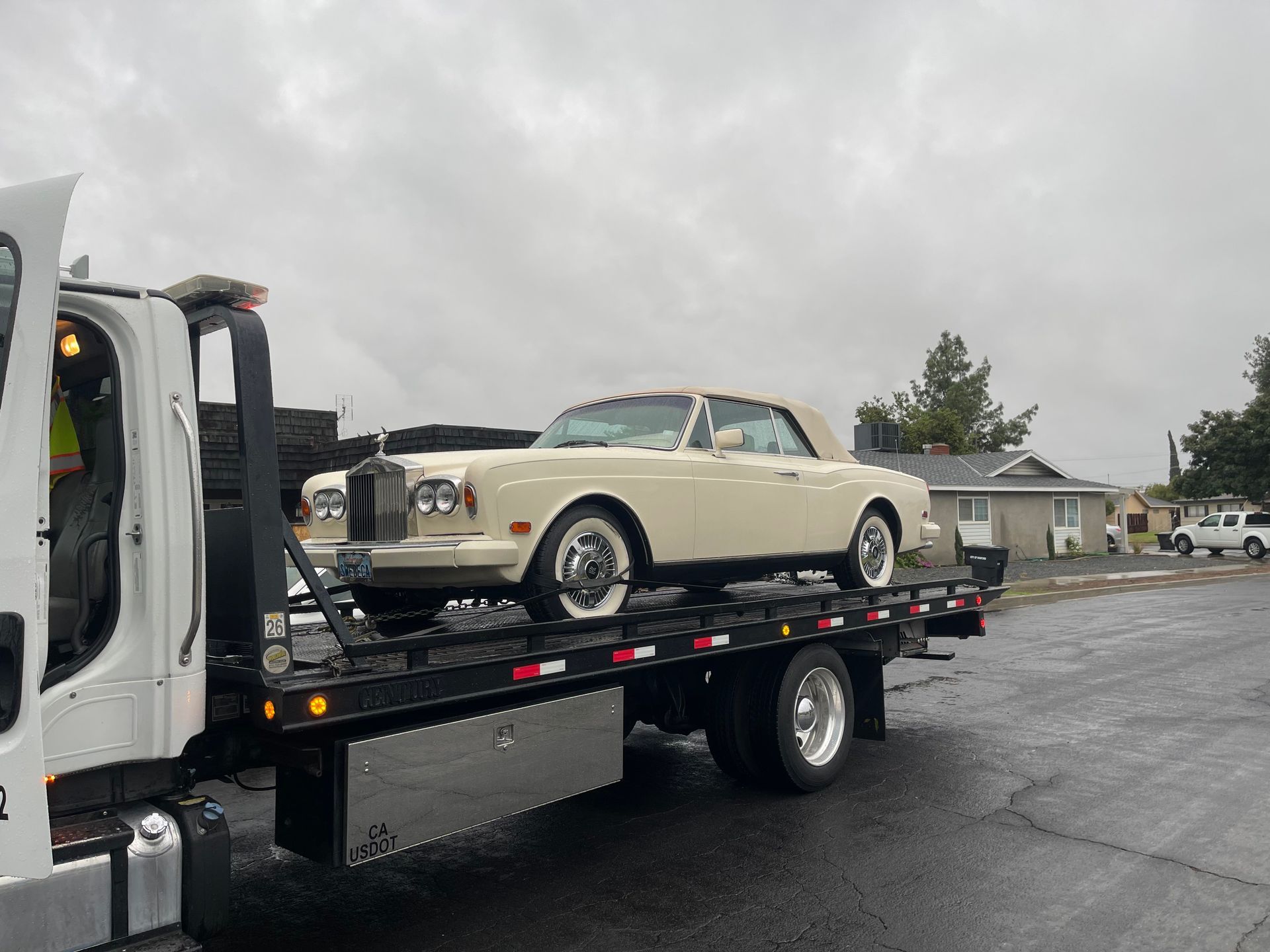 Cream Rolls-Royce convertible on a tow truck, overcast day.