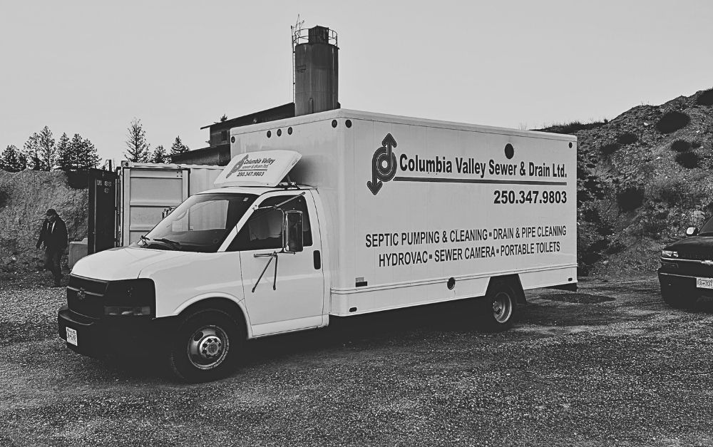 A white van is parked in a gravel lot in front of a building.