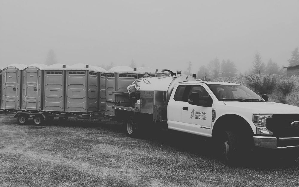 A black and white photo of a truck pulling a trailer of portable toilets.